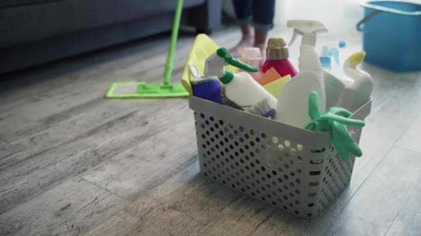 Panier plein d'éponges et de produits chimiques ménagers avec femme nettoyant le sol avec une serpillière — Video