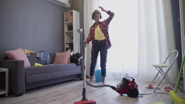 Mulher usando aspirador de pó ouvir música e dançar com fones de ouvido — Vídeo de Stock