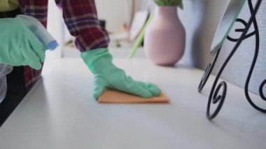 Masadaki tozları temizlemek için turuncu bez kullanan genç bir kadın.