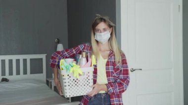 Yüzünde maske, sepet dolusu sünger ve ev yapımı kimyasallar olan kadın kameraya bakar.