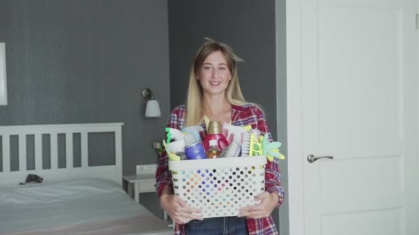 Mujer con la cesta llena de esponjas y productos químicos del hogar mira a la cámara — Vídeo de stock