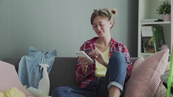 Hermosa mujer joven está descansando en el sofá después de limpiar y usar el teléfono — Vídeos de Stock