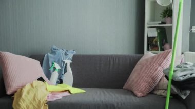 Eldivenli yorgun bir kadın kanepede oturuyor, ev temizliği yaptıktan sonra dinleniyor.