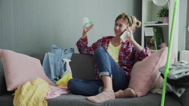 Mooie jonge vrouw rust op de bank na het schoonmaken en praten aan de telefoon — Stockvideo