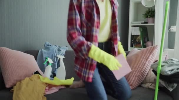 Exhausted woman in gloves sitting on sofa, relaxing after house cleaning work — Stock Video