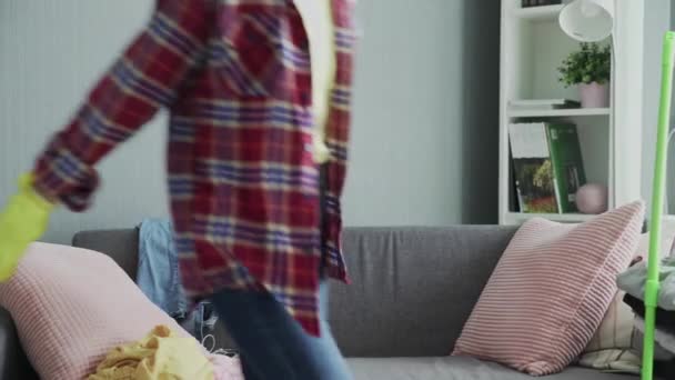 Wanita tersenyum dengan sarung tangan duduk di sofa, bersantai setelah membersihkan rumah — Stok Video