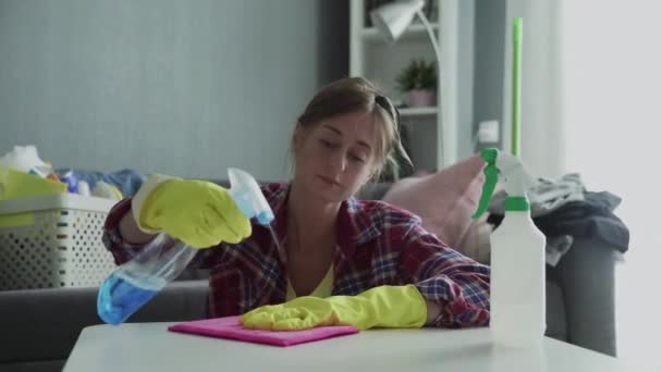 Молодая женщина с помощью розовой губки удаляет пыль со стола — стоковое видео