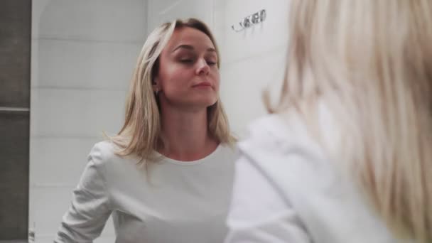 Элегантная молодая женщина смотрит на зеркало в ванной комнате — стоковое видео