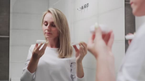 Жінка наносить крем і дивиться у дзеркало насолоджується природною красою і здоровим — стокове відео