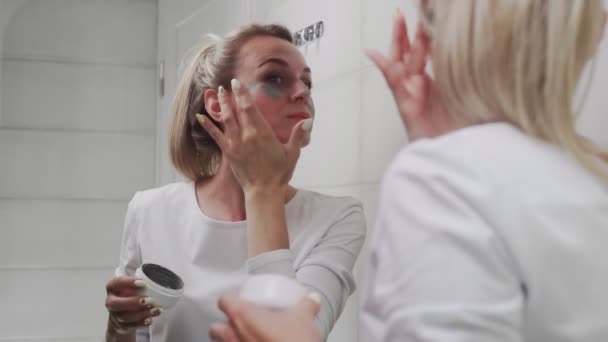 Mujer aplicando máscara en su cara mirando en el espejo — Vídeos de Stock