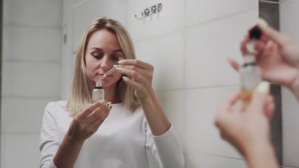 Женщина наносит лосьон или масло и смотрит в зеркало — стоковое видео