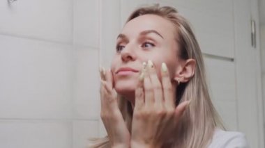 Krem süren ve aynaya bakan kadın doğal güzelliğin ve sağlığın tadını çıkarıyor.