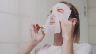 Yüzüne maske takıp aynaya bakan bir kadın.