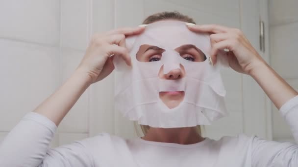 Κοντινό πλάνο της γυναίκας εφαρμογή μάσκα στο πρόσωπό της και κοιτάζοντας την κάμερα — Αρχείο Βίντεο