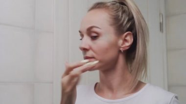 Aynaya bakarak yüzüne kilden maske takan bir kadın.