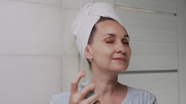 Close up Mulher adulta com uma toalha na cabeça aplicando spray de água para hidratação da pele — Vídeo de Stock