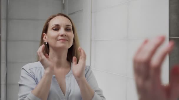 Взрослая белая женщина перед зеркалом в ванной. Умывание лица, кожа, оздоровление — стоковое видео