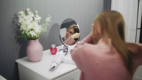 Gyönyörű fiatal nő használ hajszárítót, miközben belenéz a tükörbe a szobában. — Stock videók