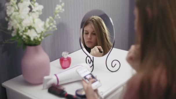 Jonge mooie vrouw houden borstel van toepassing blush poeder en met behulp van smartphone — Stockvideo