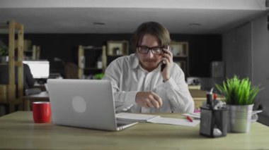 Müdür telefonda konuşuyor ve ofiste yazı yazıyor.
