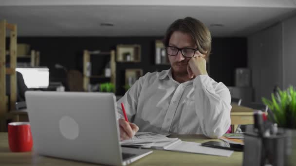 Молодий менеджер дивиться документи, що сидять за столом в офісі — стокове відео