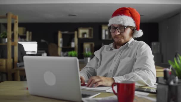 Mladý unavený manažer pracuje a pije čaj v kanceláři na Vánoce — Stock video