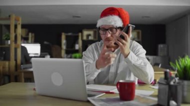 Genç yönetici çalışıyor ve yılbaşında ofiste akıllı telefondan konuşuyor.
