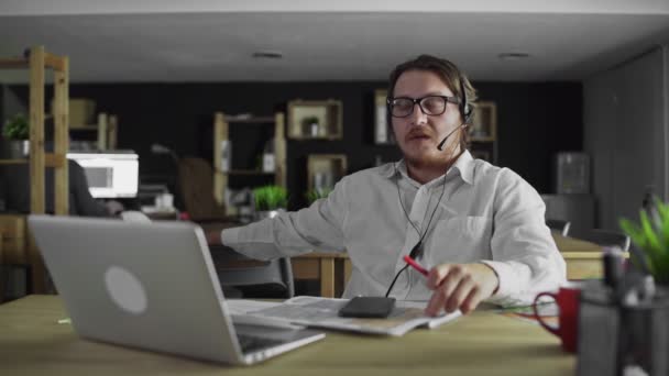 Młody menedżer w słuchawkach pracuje patrząc w smartfonie w biurze — Wideo stockowe
