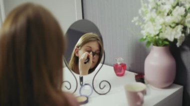 Makyaj yapan ve çay içen güzel bir kadın. Güzel kız aynaya bakıyor ve büyük bir fırçayla kozmetik uyguluyor..