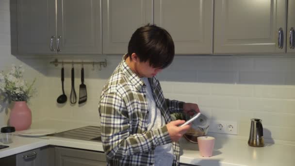 Asiático homem usando smartphone e beber café na cozinha em casa — Vídeo de Stock