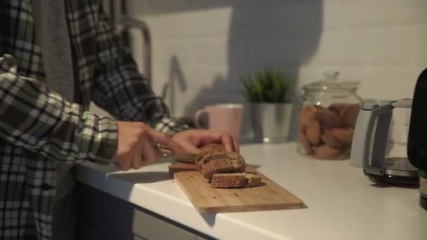 Zbliżenie krojenia brązowego chleba na desce do krojenia. Człowiek kroi ciemny chleb z nasionami — Wideo stockowe