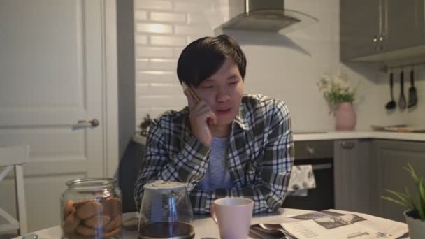 Asiatisk man pratar på mobiltelefon i köket hemma — Stockvideo