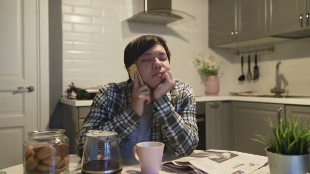 Сонный азиат разговаривает по мобильному телефону на кухне дома — стоковое видео