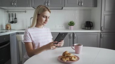 Çekici bir kadın mutfakta kahvaltı yaparken tablet kullanıyor.