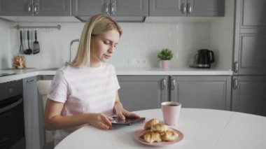 Mutfakta kahvaltı yaparken tablet kullanan üzgün kadın.