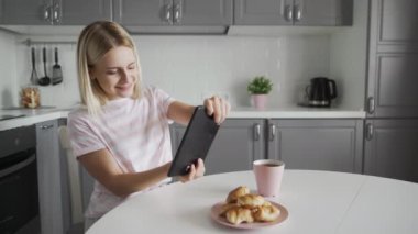 Çekici kadın, mutfakta kahvaltı ederken tablet üzerinde video oyunu oynuyor.