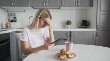 Mutfakta kahvaltı yaparken tablet kullanan üzgün kadın.