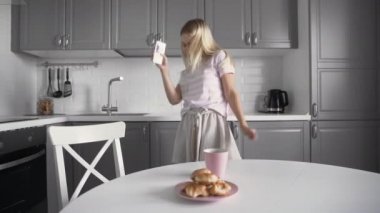 Kulaklık takmış, müzik dinleyen bir kadın mutfakta akıllı telefon tutuyor.
