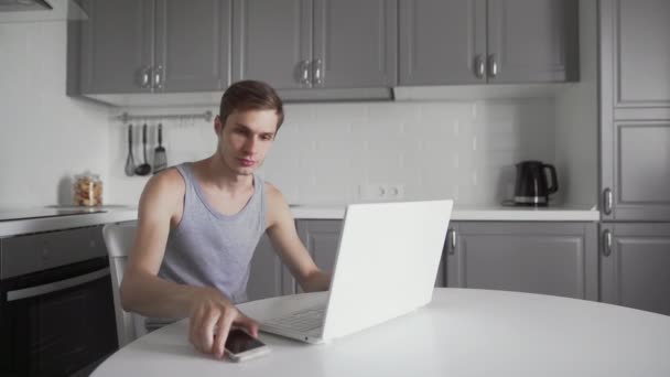 Young man working on laptop computer and using phone at home. Busy business man — Stock Video