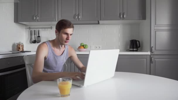 Jeune pigiste avec écouteurs travaillant sur ordinateur portable et boire du jus — Video