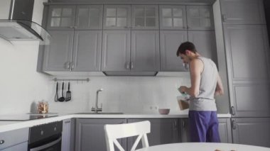 Genç adam mutfakta kahvaltı hazırlıyor. Bir kaseye mısır gevreği döker.