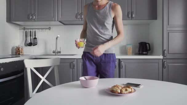 Молодий чоловік снідав на кухні. Чоловік п'є сік і використовує телефон — стокове відео