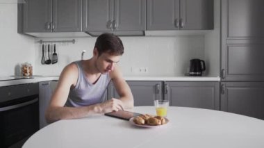 Genç adam evde mutfakta otururken dijital tablet kullanıyor.