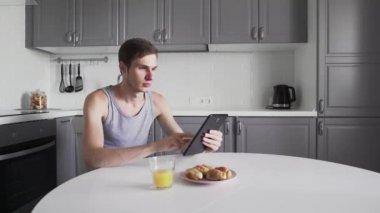 Tablet bilgisayarında sohbet eden ve mutfakta meyve suyu içen bir adam.