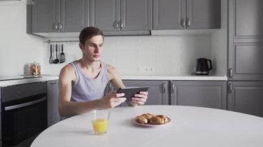 Genç adam evde mutfakta otururken video oyunu oynamak için dijital tablet kullanıyor