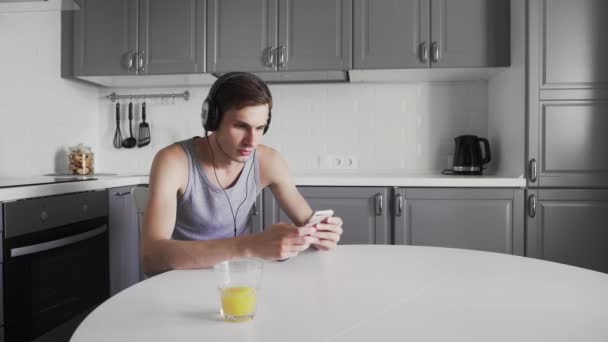 Jeune homme assis à la table et écoutant de la musique dans les écouteurs — Video
