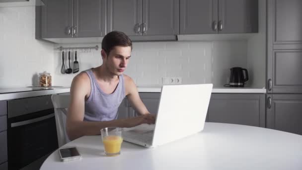 Молодой человек работает на ноутбуке и пользуется телефоном дома. Вдумчивый бизнесмен — стоковое видео