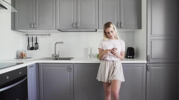 台所のチェック電話で朝の若い女の子。女性は携帯電話を使って友達とチャットする。スマートフォンにメッセージを送る女の子. — ストック動画