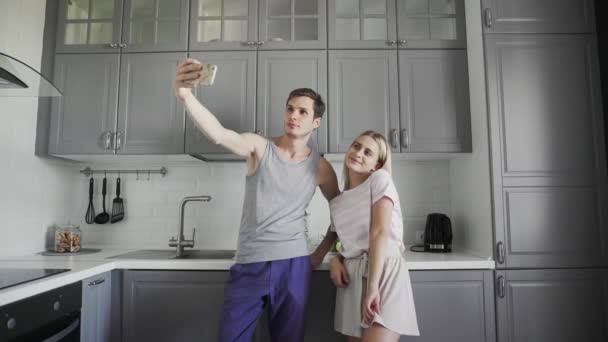 Jeune couple souriant, posant et prenant un selfie dans la cuisine le matin — Video