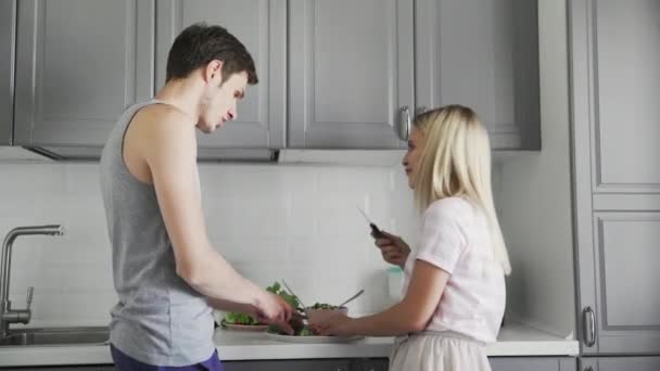 Milující pár krájí zeleninu a dělá salát společně k obědu v kuchyni — Stock video